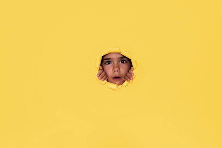 Surprised cute 6-7 years old girl looking from the round shaped hole in the colored cardboard, empty space for advertising text in torn paper, background textureの写真素材
