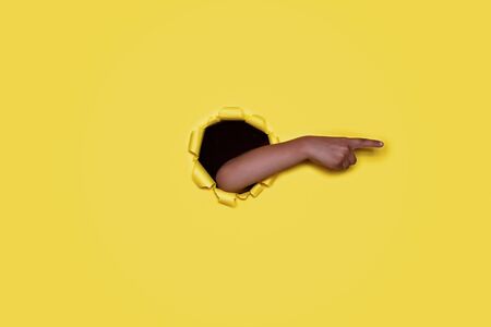Kid hand stretching from the round shaped hole in the colored cardboard and pointing to the left, empty space for advertising text in torn paper, background textureの写真素材