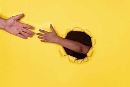 Kid and adult hands reaching towards each other from the round shaped hole in the colored cardboard, empty space for advertising text in torn paper, background texture, help and support conceptの写真素材