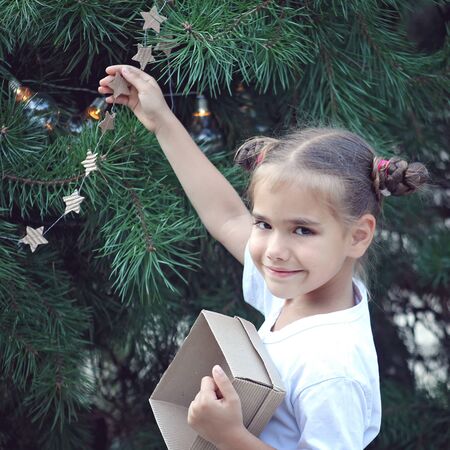 Cute school girl holding crafted Christmas garland made from used paper box, zero waste lifestyle, reuse and ecological decorationの写真素材