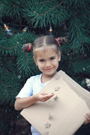 Cute school girl holding crafted Christmas garland made from used paper box, zero waste lifestyle, reuse and ecological decorationの写真素材