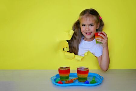 Girl having fun at birthday party and holding a plate with colored jelly looking through a paper hole, glass with traffic light colored jelly, holiday and celebration concept. Indoor portraitの写真素材