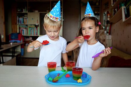 Happy sister and brother having fun at birthday party, glass with traffic light colored jelly, holiday and celebration concept. Indoor portraitの写真素材