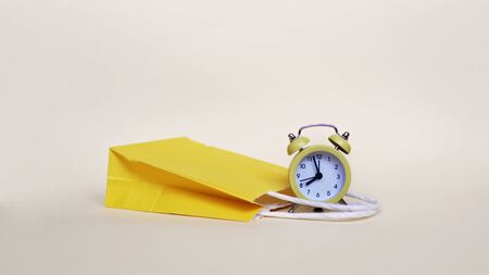 Yellow shopping bag and yellow alarm clock over light background, shopping and sales concept