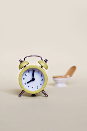 Yellow alarm clock and white toilette bowl over light background, healthcare and wasting time...