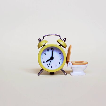 Yellow alarm clock and white toilette bowl over light background, healthcare and wasting time conceptの写真素材
