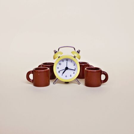 Yellow alarm clock and several tiny brown cups with coffee over light background, food and drink, morning and active working day conceptの写真素材