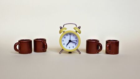 Yellow alarm clock and several tiny brown cups with coffee over light background, food and drink, morning and active working day concept, banner formatの写真素材