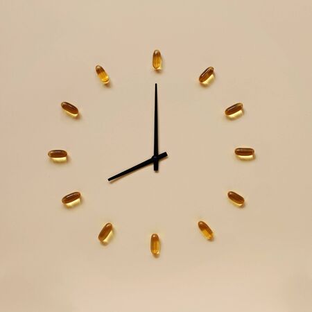 Yellow pills and black indicators placing like clock face over light background, health care and medicine, vitamins and healthy lifestyle conceptの写真素材