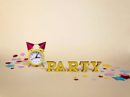 Party greeting poster with yellow alarm clock with celebration hats and different colorful paper decoration, holidays and celebration conceptの写真素材