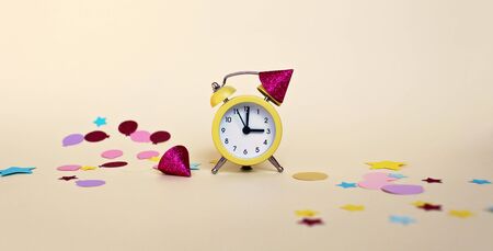Party greeting poster with yellow alarm clock with celebration hats and different colorful paper decoration, holidays and celebration conceptの写真素材
