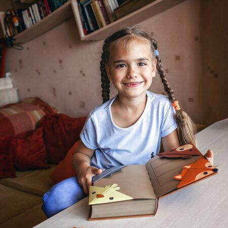 Smart cute kid girl holding a book with crafted paper corner bookmark, creative ideas for kids, fun and easy, indoorの写真素材