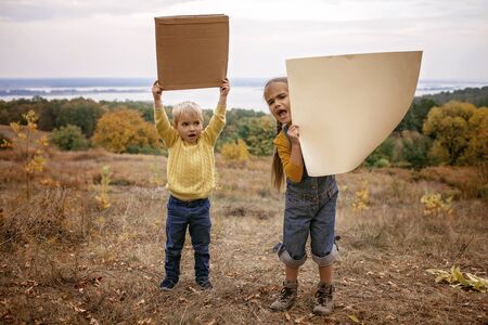 Young kids holding a poster over beautiful autumn nature background, save the planet, no plastic, school movement, eco concept, mockup for your message, outdoor lifestyleの写真素材