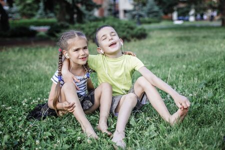 Pretty 6-7 years old preschool girl and boy sharing headphones to listen music together at sunset in the street, music and little star concept, outdoor emotional portraitの写真素材