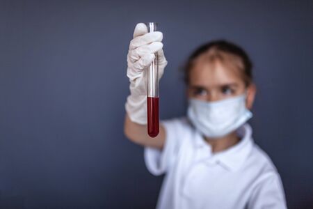Cute kid wearing respirator mask and medicine gloves playing in a doctor and holding a blood test result for the new rapidly spreading Coronavirus over blue background, health and medicine conceptの写真素材