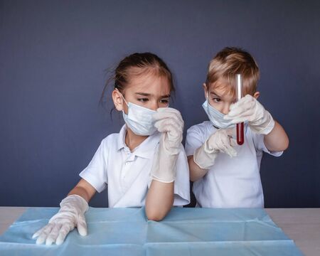 Cute kid wearing respirator mask and medicine gloves playing in a doctor and holding a blood test result for the new rapidly spreading Coronavirus over blue background, health and medicine conceptの写真素材