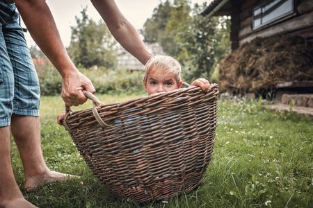 Cute little boy having fun together with his father and playing with hurdled basket on the backyard of old country house in village at summer, happy summertime in countryside, outside emotional lifestyleの写真素材
