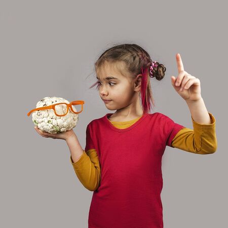 Freakish kid with pinky hair in eyeglasses holds misshapen wrong color fruits and vegetables, giants, with tiny spots and scars, isolated over white background, garbage and waste food trend conceptの写真素材