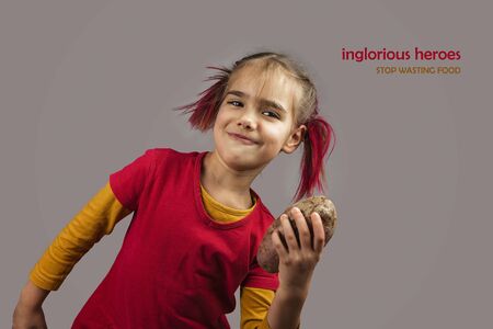 Freakish kid with pinky hair in eyeglasses holds misshapen wrong color fruits and vegetables, giants, with tiny spots and scars, isolated over white background, garbage and waste food trend conceptの写真素材