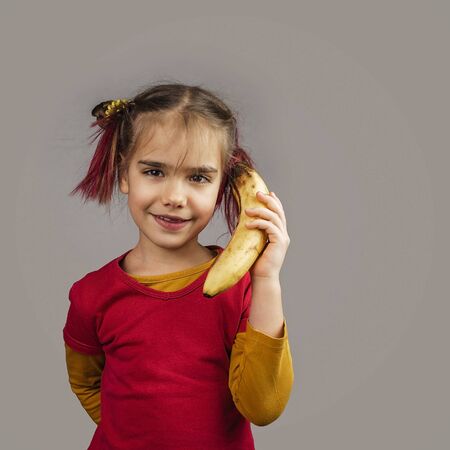 Freakish kid with pinky hair in eyeglasses holds misshapen wrong color fruits and vegetables, giants, with tiny spots and scars, isolated over white background, garbage and waste food trend conceptの写真素材