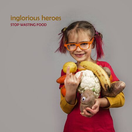 Freakish kid with pinky hair in eyeglasses holds misshapen wrong color fruits and vegetables, giants, with tiny spots and scars, isolated over white background, garbage and waste food trend conceptの写真素材