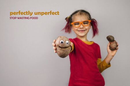 Freakish kid with pinky hair in eyeglasses holds misshapen wrong color fruits and vegetables, giants, with tiny spots and scars, isolated over white background, garbage and waste food trend conceptの写真素材