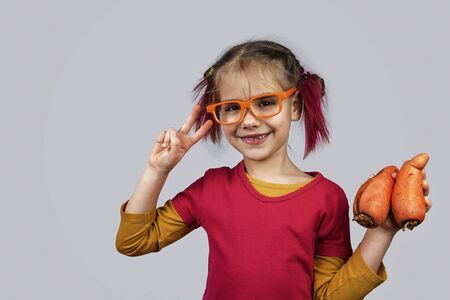 Freakish kid with pinky hair in eyeglasses holds misshapen wrong color fruits and vegetables, giants, with tiny spots and scars, isolated over white background, people and waste food trend conceptの写真素材
