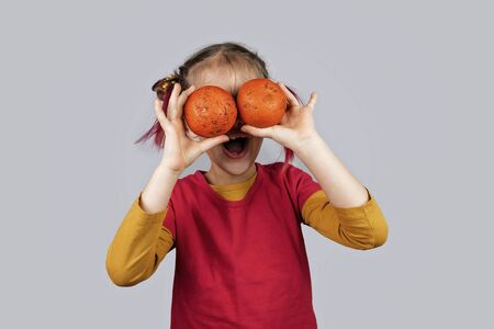 Freakish kid with pinky hair in eyeglasses holds misshapen wrong color fruits and vegetables, giants, with tiny spots and scars, isolated over white background, people and waste food trend conceptの写真素材
