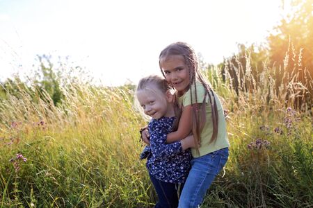 Happy adorable kids having fun and hugs together in the green grass with flowers on the meadow, happy golden sunset at summer, summertime and childhood, emotional outdoor lifestyleの写真素材