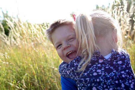 Happy adorable kids having fun and hugs together in the green grass with flowers on the meadow,...