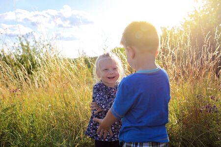 Happy adorable kids having fun and hugs together in the green grass with flowers on the meadow, happy golden sunset at summer, summertime and childhood, emotional outdoor lifestyleの写真素材