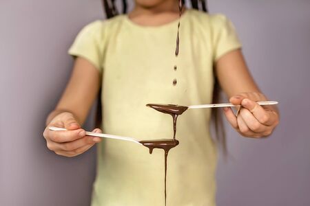 Stylish school girl pouring liquid hot chocolate with teaspoon, there is never much chocolate, healthy food concept, studio shot, image for world chocolate dayの写真素材