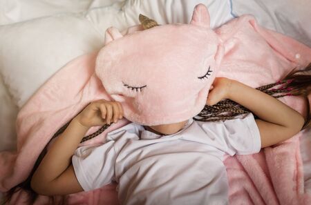 Top view of cute awaking school girl with her toy animals wearing in light pink pajama with unicorn hoody, happy family concept, indoor horizontal portraitの写真素材