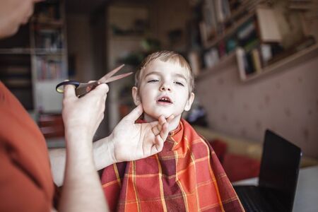 Middle aged father cutting hair to his little son by himself at home looking video broadcast on laptop, hairstyle online class, stay home and life during lockdownの写真素材