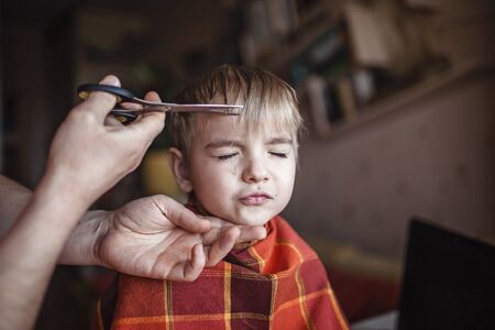 Middle aged father cutting hair to his little son by himself at home looking video broadcast on laptop, hairstyle online class, stay home and life during lockdownの写真素材