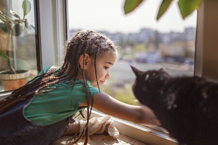 Cute girl helping to care for home plants on the balcony window, plant parents concept, home gardening, green environment at homeの写真素材