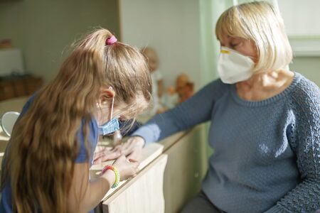 Multigenerational relations, care about seniors in new normal life, grandmother playing in beauty salon and helping grandkid to do makeup, they are wearing in medical respirators, social distance ruleの写真素材