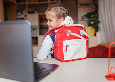 Back to school, new normal education. Cute girl in school uniform greeting somebody via video call...