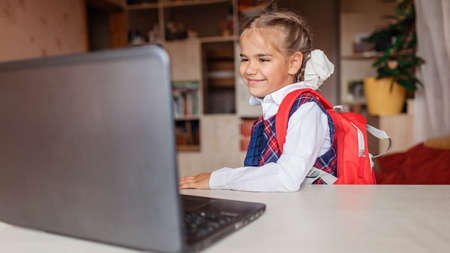 Back to school, new normal education. Cute girl in school uniform greeting somebody via video call and showing her new backpack. Social distance learning and new guidanceの写真素材