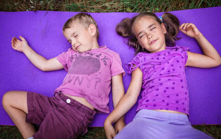 Active healthy weekend. Happy kids, boy and girl, having rest and fun on the purple yoga mat during...