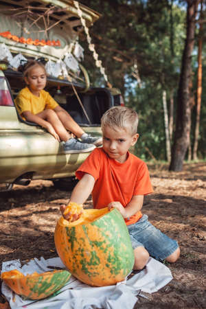 Alternative safe celebration. Cute kids preparing Halloween party in the trunk of car with carved pumpkin, spider net, ghosts and other decoration for Halloween, autumn outdoor.の写真素材