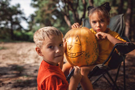 Alternative safe celebration. Cute kids preparing Halloween party in the trunk of car with carved pumpkin, spider net, ghosts and other decoration for Halloween, autumn outdoor.の写真素材