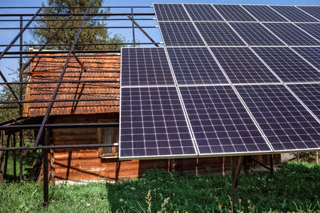 A big solar panel on the roof on the old wooden house at mountain countryside, past and future, ecological technology in the village, warm summer dayの写真素材