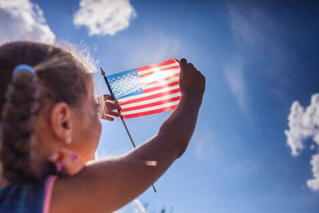 Patriot and National Flag day celebration. Cute little patriot sitting on the meadow and holding the...