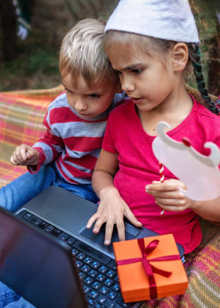 New normal online Christmas celebration. Cute sibling using laptop and festive fun props to...
