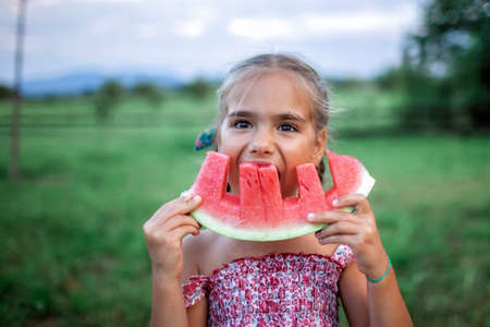 Healthy summer food. Cute kid biting a slice of watermelon in the backyard of farmhouse, happy summertime, countryside, outdoor lifestyleの写真素材