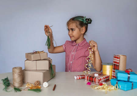 DIY decoration. Cute girl making a choice between common wrapped box with plastic bow and homemade wrapping with natural materials, pine needles, brunches and citrus slices, zero waste holidaysの写真素材