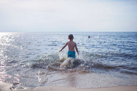Happy sibling running into the sea and splashing in sunset light, lots of fun and happiness, summer lifestyleの写真素材