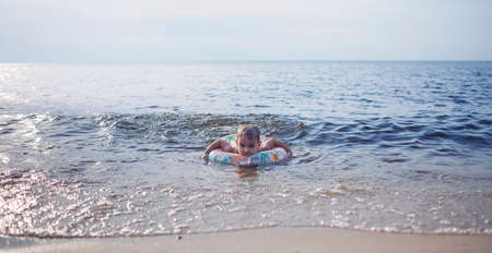 Little boy with flotation ring swimming at sea in sunset light, lots of splashes and happiness, summer lifestyleの写真素材