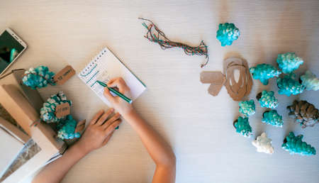Cute girl preparing DIY gifts and signing tags to parents and family for Christmas, a green cone as...
